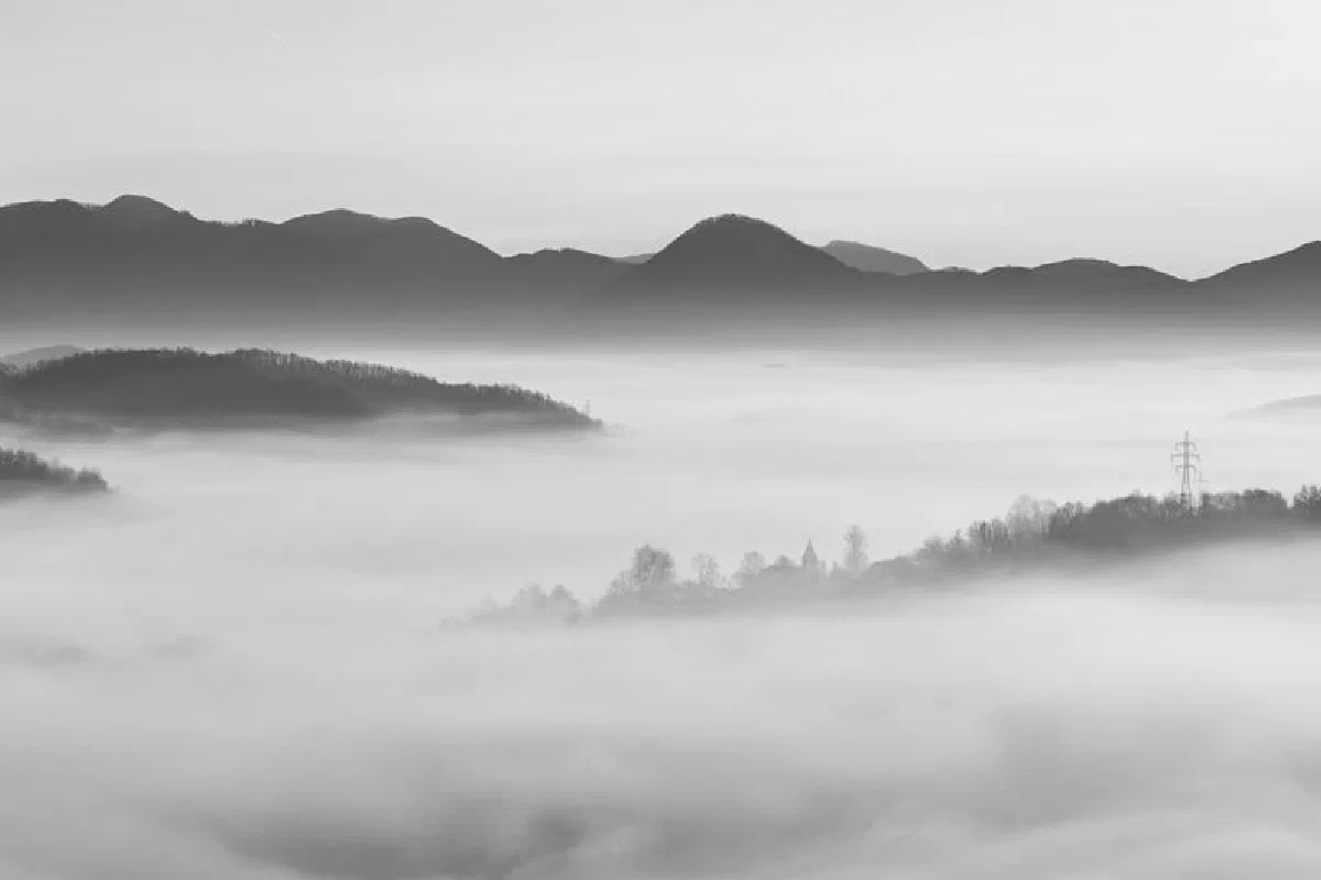 Tranquil black and white landscape featuring misty valleys and layered mountain silhouettes.