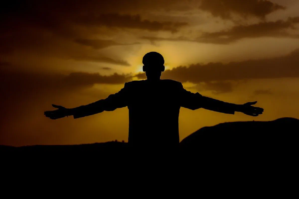 A solitary silhouette of a man stretching his arms against a vivid golden sunset, exuding calm and strength.