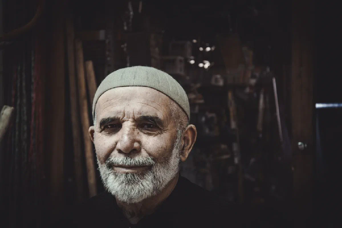 Close-up portrait of a senior man with a gray beard and cap, smiling warmly.