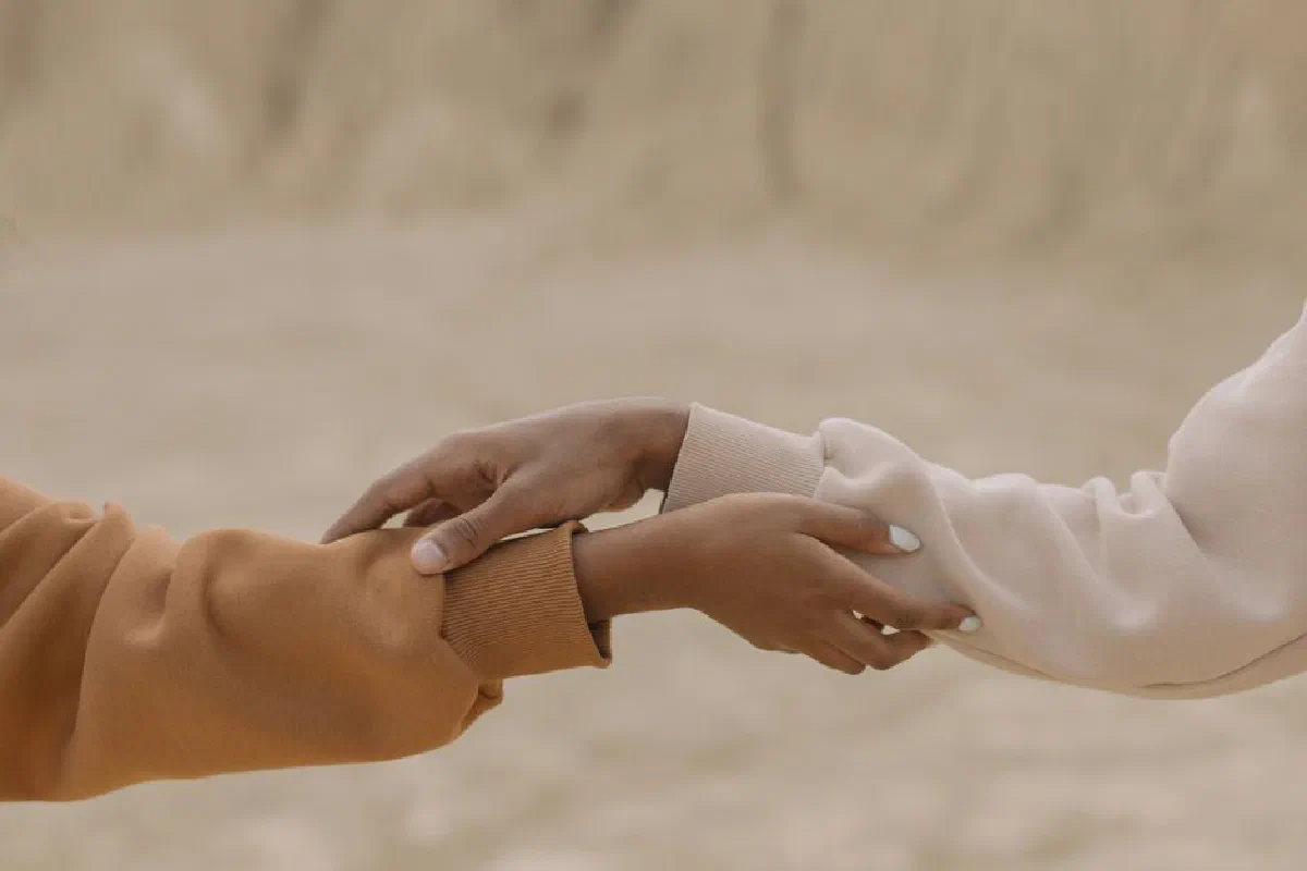 Close-up view of two hands reaching and holding each other against a muted background, symbolizing connection.