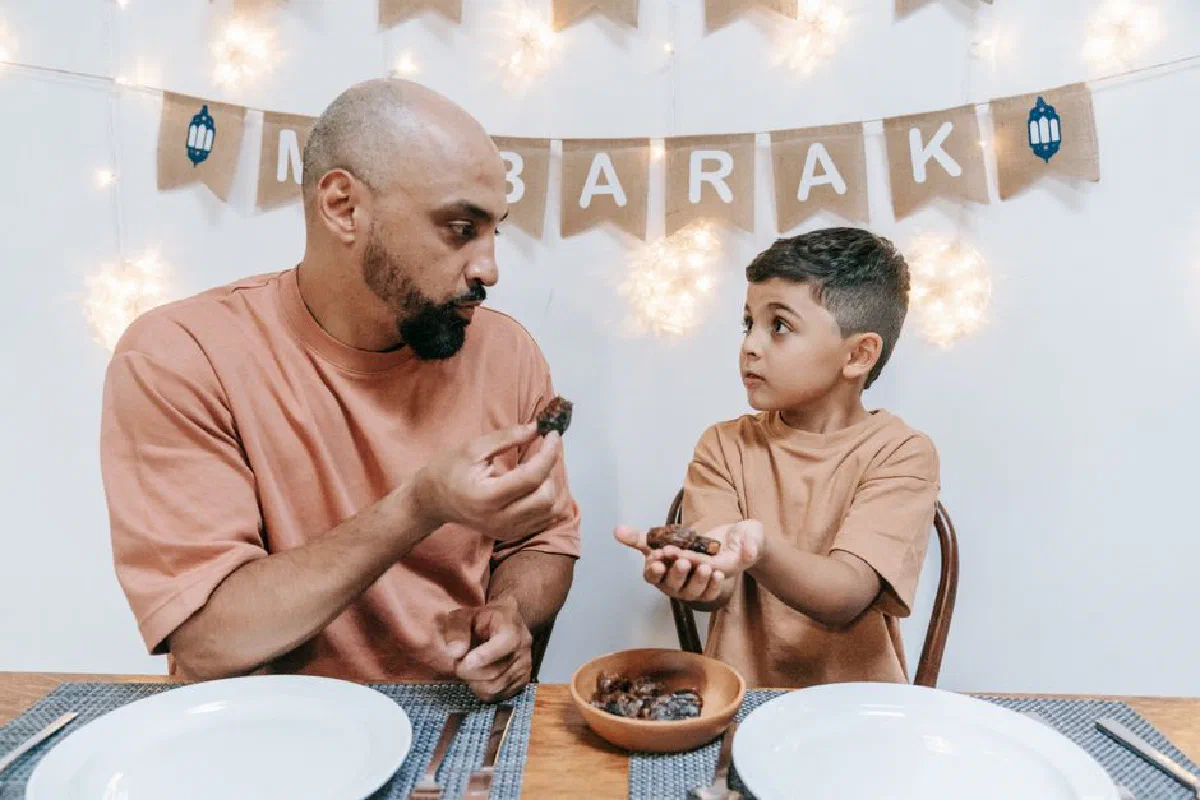 A father and son share dates during an Eid Mubarak celebration indoors.