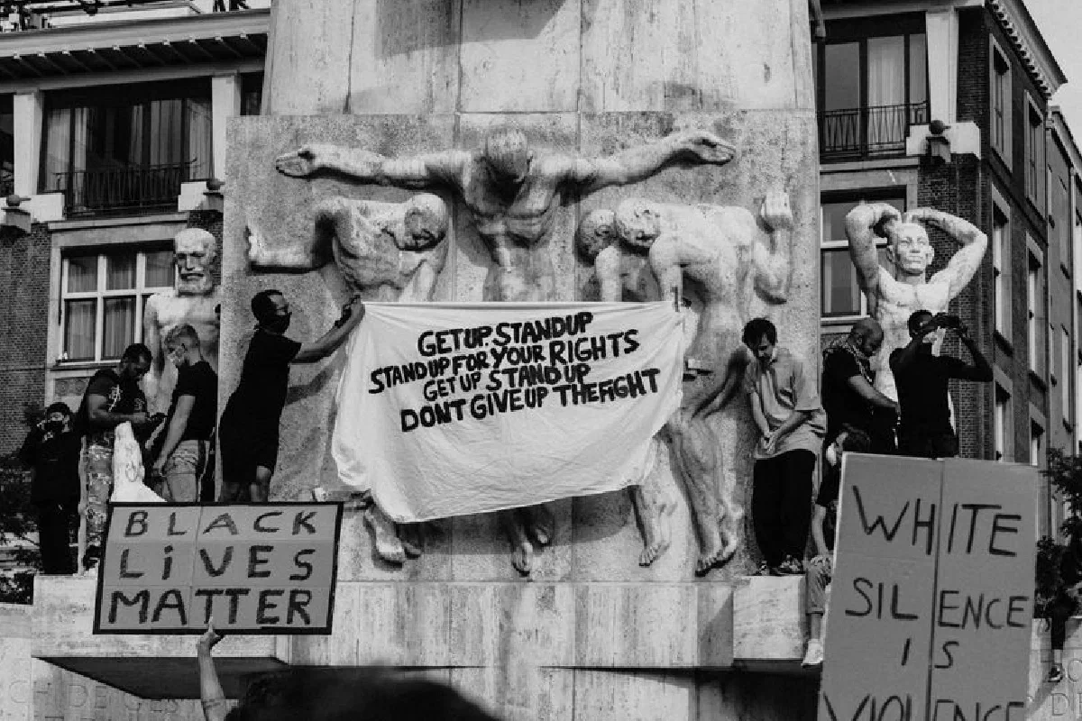 Black and white of crowd of people standing on city street with carton boards during social protest