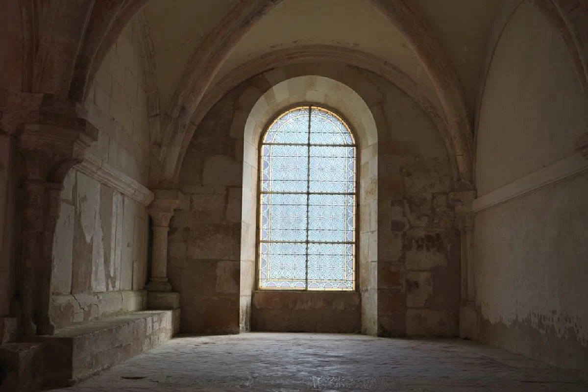 A serene stone interior with a gothic arched window in Montbard, France.