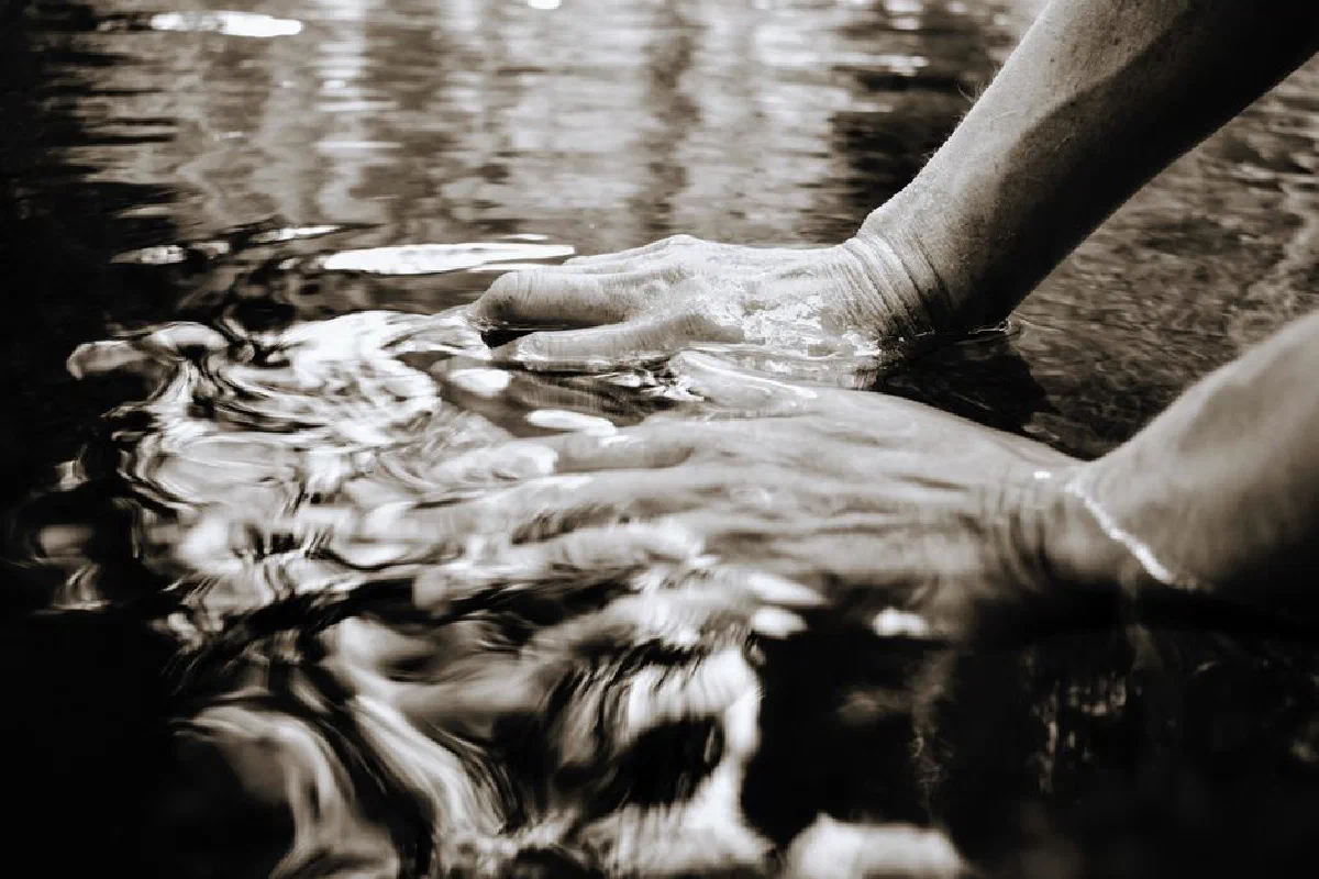 Close-up of hands interacting with rippling water, creating reflections and texture.