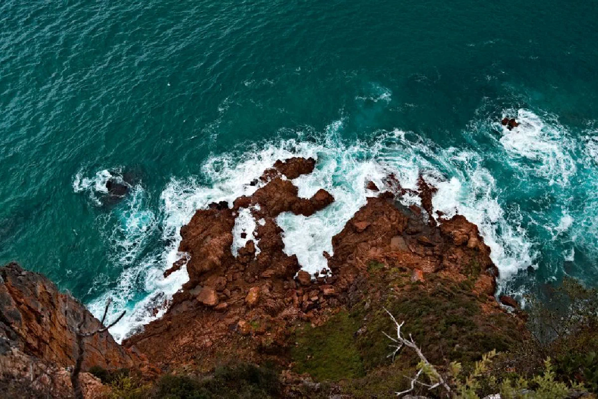 A dramatic aerial view of rugged brown cliffs and crashing sea waves.