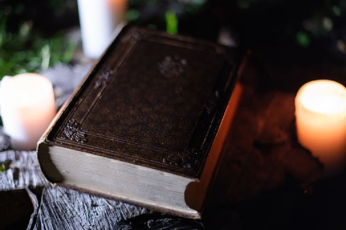 A vintage book on a wooden table surrounded by lit candles, creating a warm, atmospheric scene.