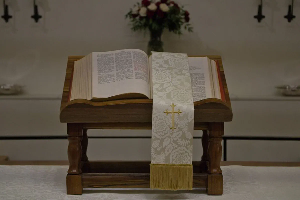 A close-up of an open Bible on a church altar with a cross-embroidered cloth in a religious setting.