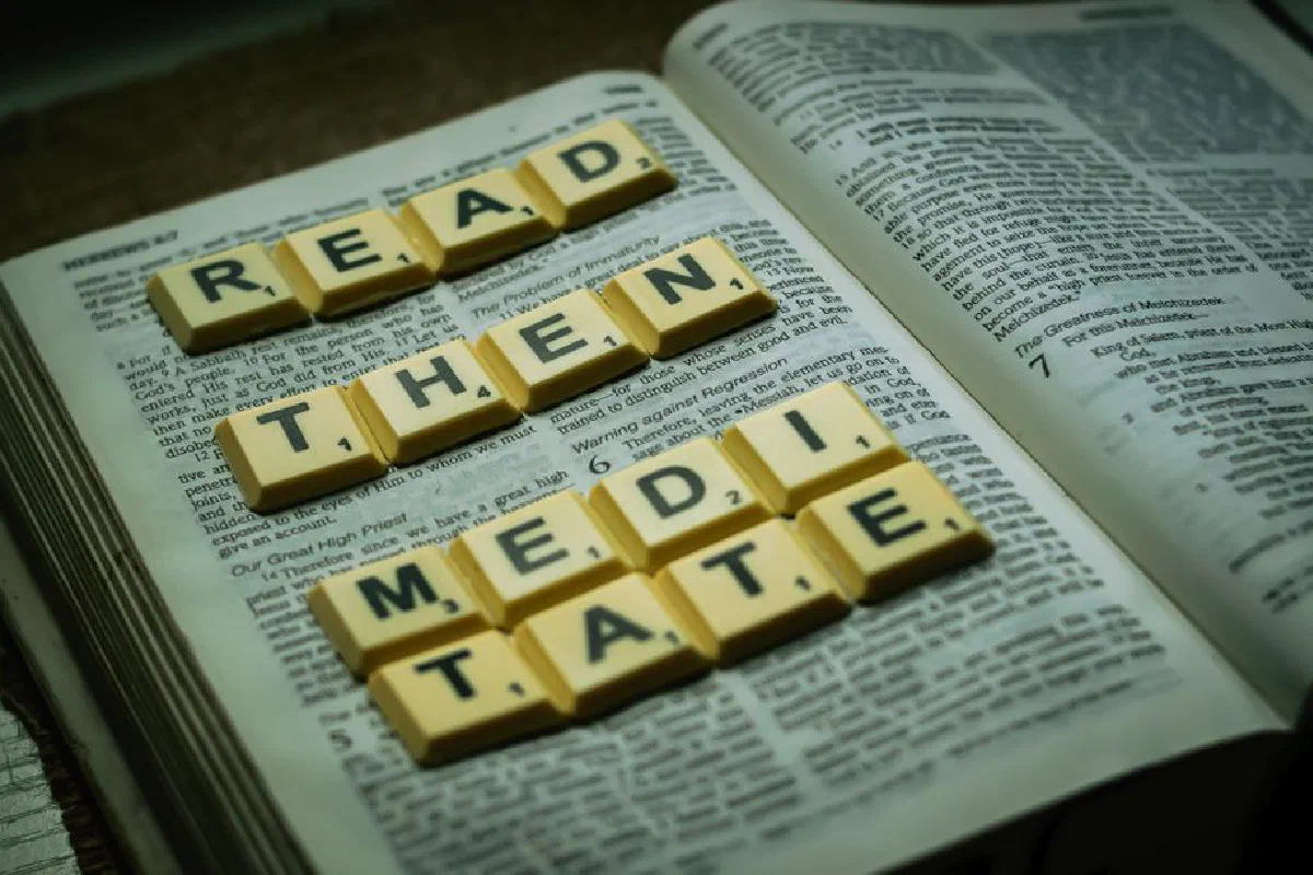 Open Bible with Scrabble tiles spelling 'Read Then Meditate' in a still life composition.