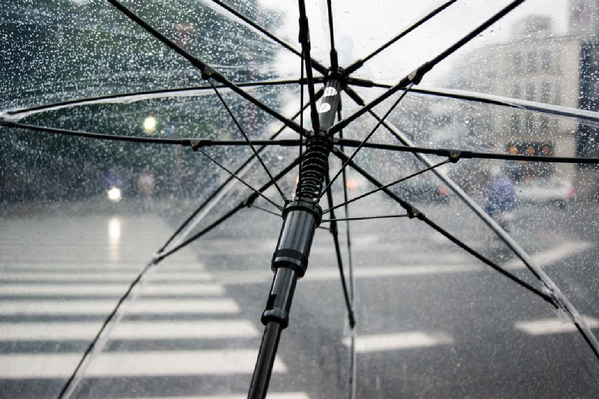 Close-up of a transparent umbrella with raindrops in an urban street setting.