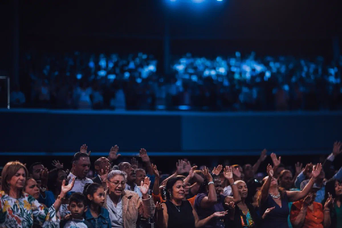 A diverse group of people raising hands in a worship setting, captured indoors.