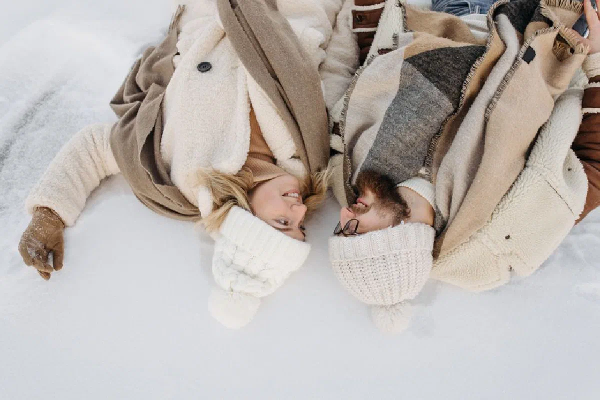Couple enjoying togetherness in winter, lying on snowy ground with warm clothing.