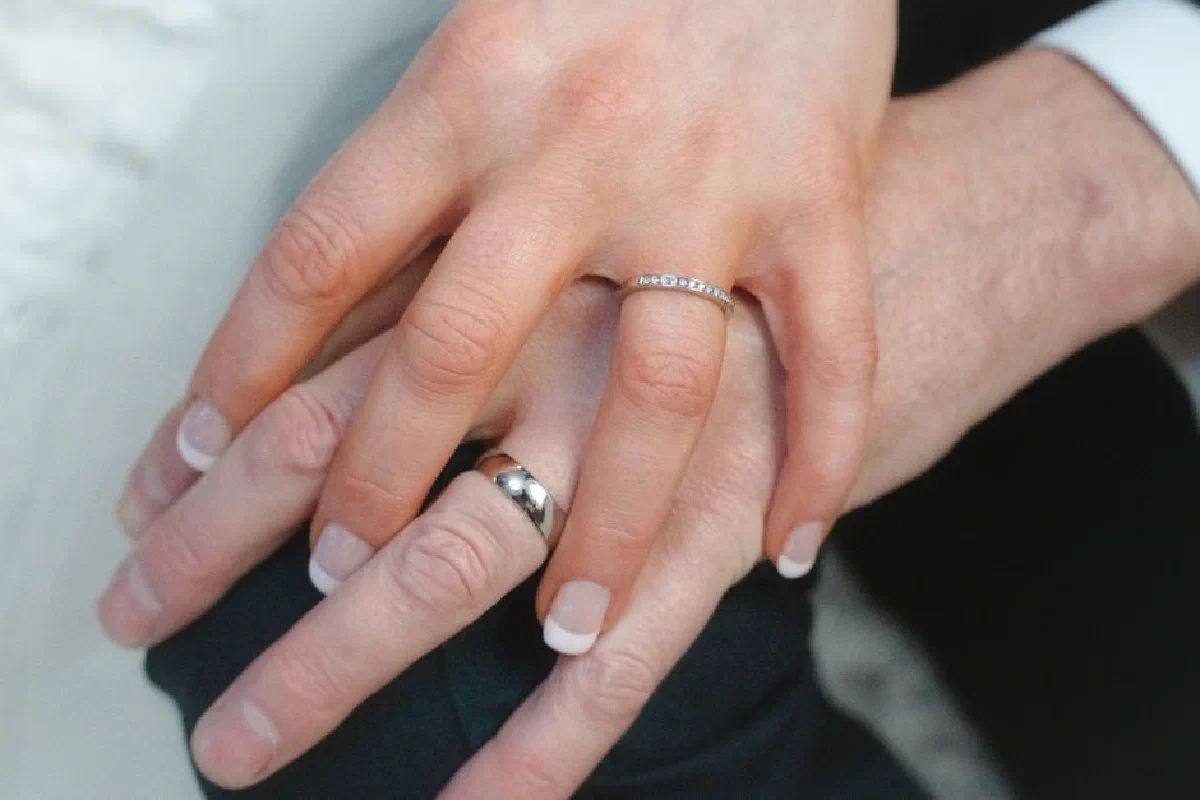 A romantic close-up showing a couple's interlocking hands with elegant wedding rings symbolizing love and commitment.