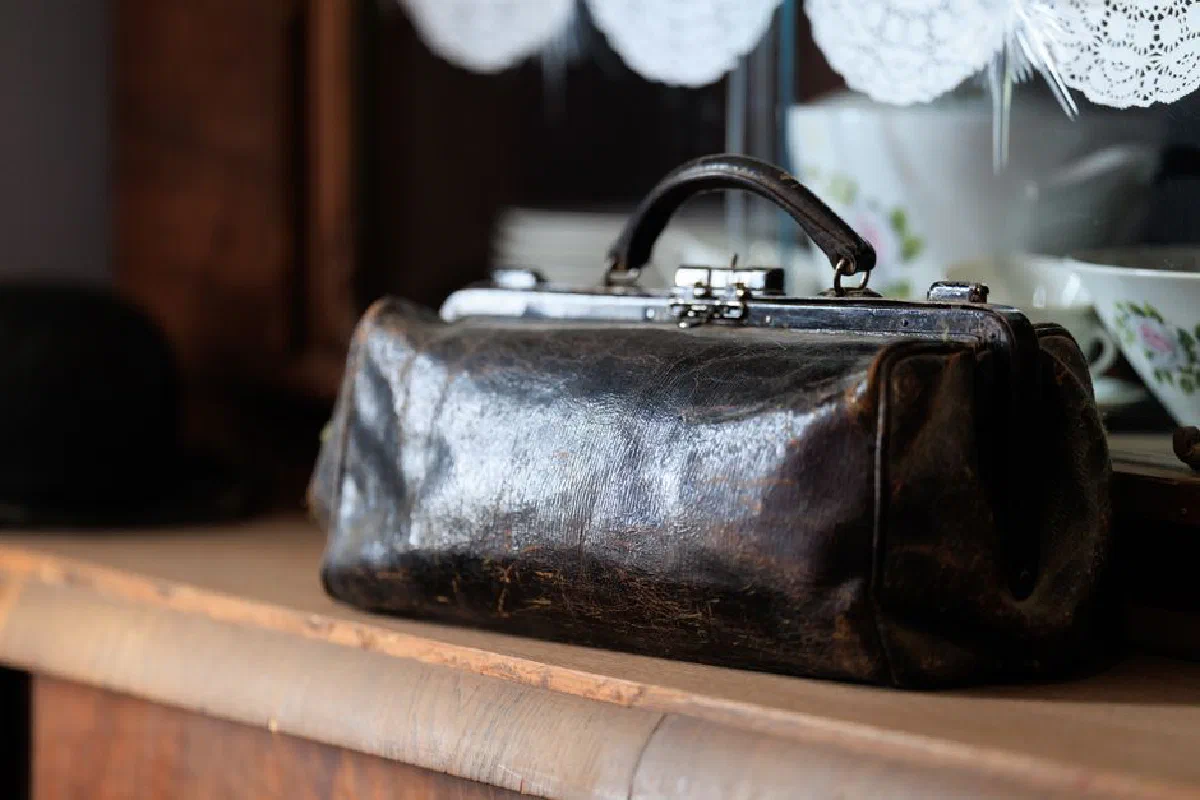 Close-up of a vintage leather bag on a wooden shelf indoors, exuding a nostalgic and classic atmosphere.