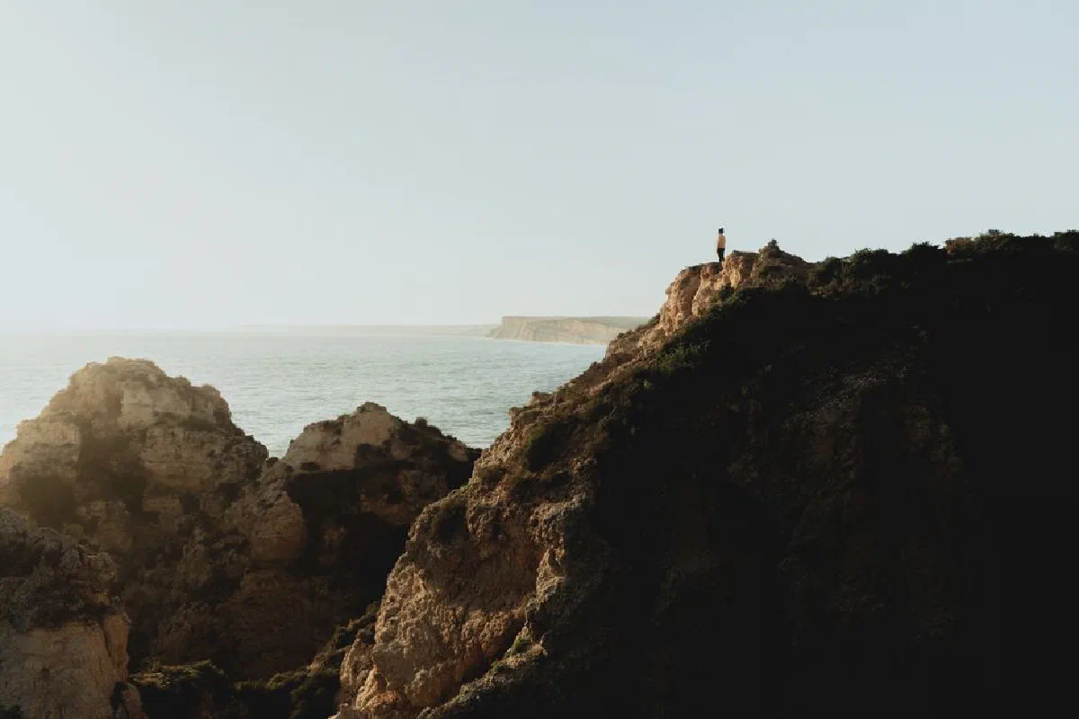 A person stands on a cliff overlooking the ocean in the Algarve region, Portugal.