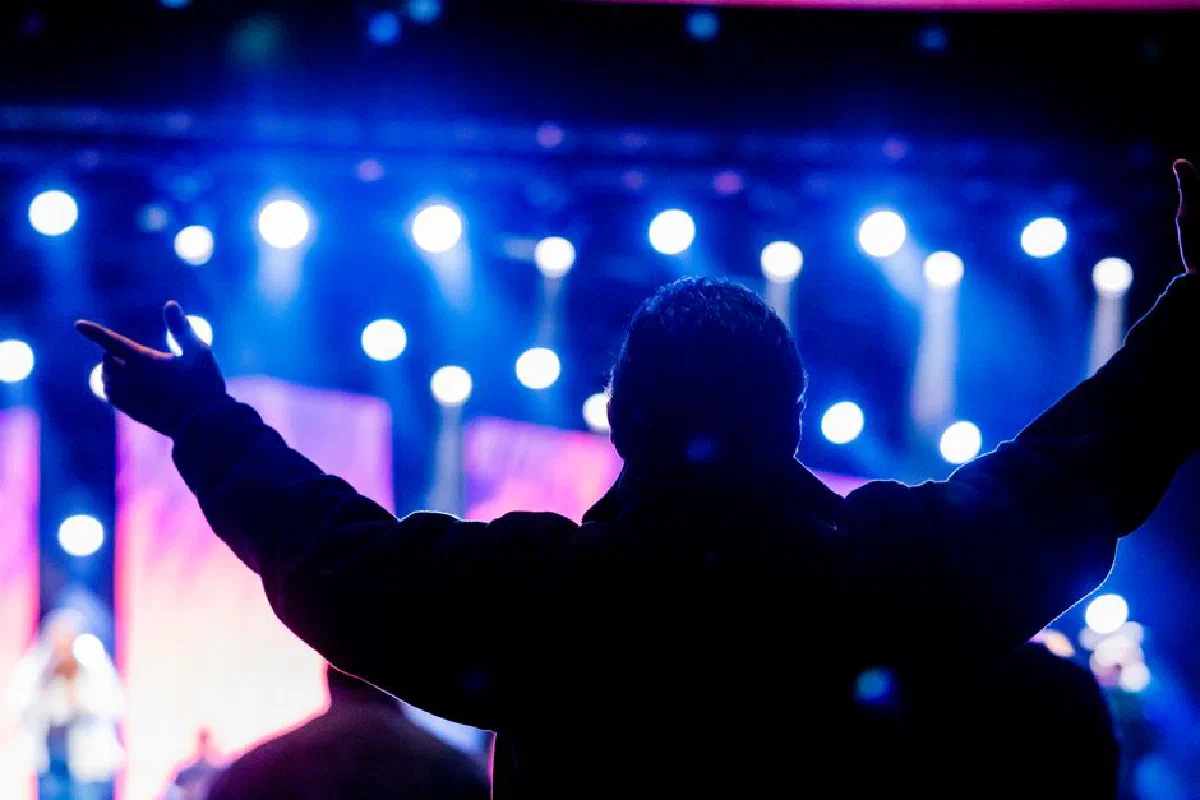 Silhouette of a person raising hands in front of bright stage lights during a live concert.