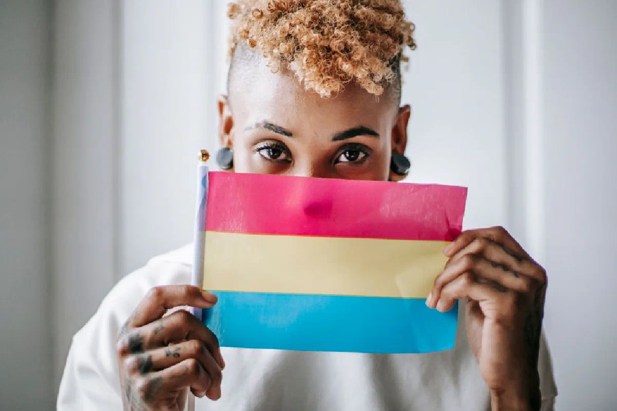 Crop anonymous African American female with curly short dyed hair demonstrating Pansexual pride flag and looking at camera