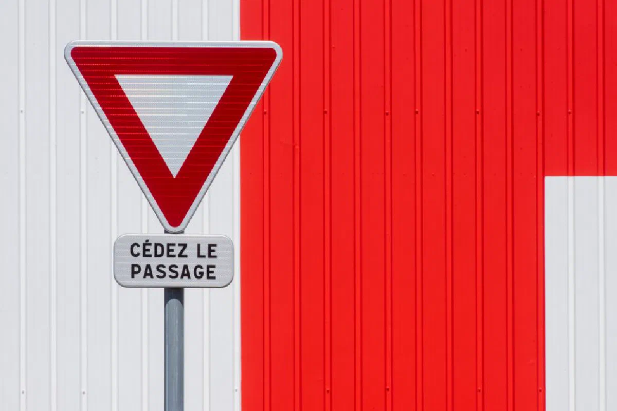 A French yield sign 'Cédez le passage' stands against a vivid red wall.