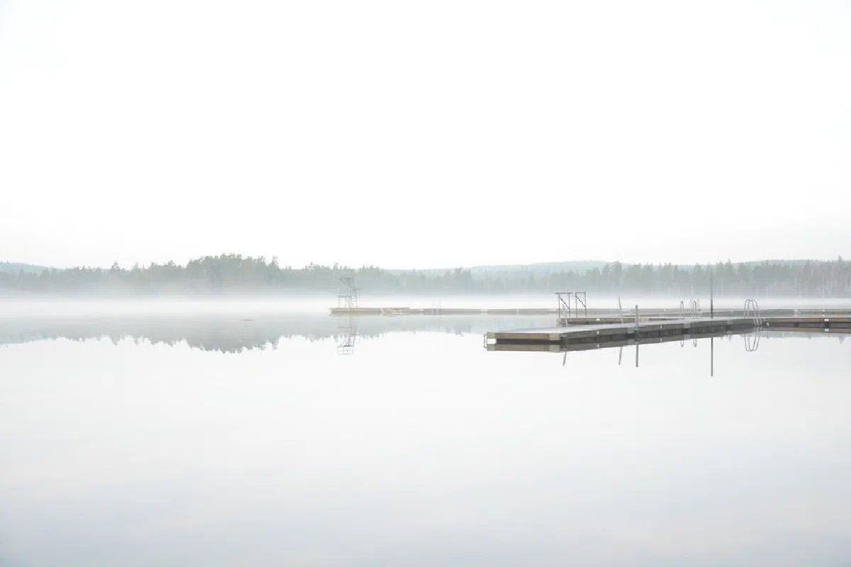 A tranquil misty lake scene with a wooden dock extending into the foggy morning.