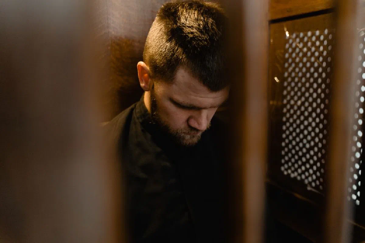 A man in a confessional booth, deep in prayer, symbolizing faith and spirituality.