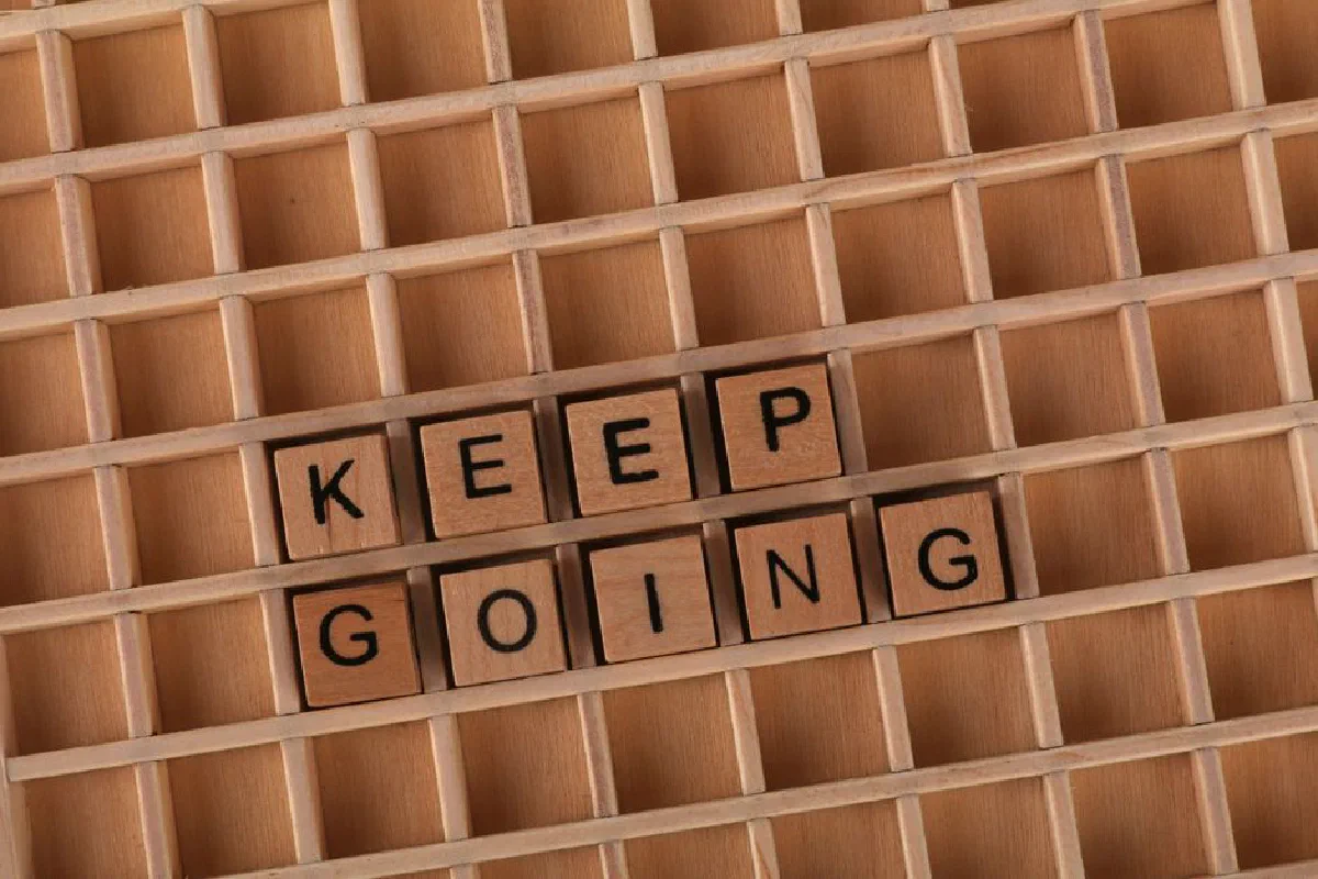 Keep going message spelled with wooden blocks on a wooden grid background.
