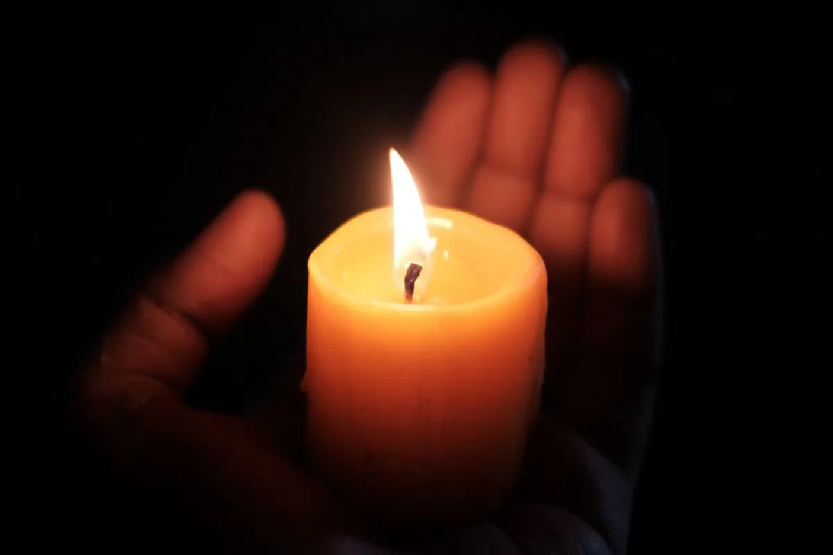 A single candle held in a human hand creates a warm, intimate glow in the dark.