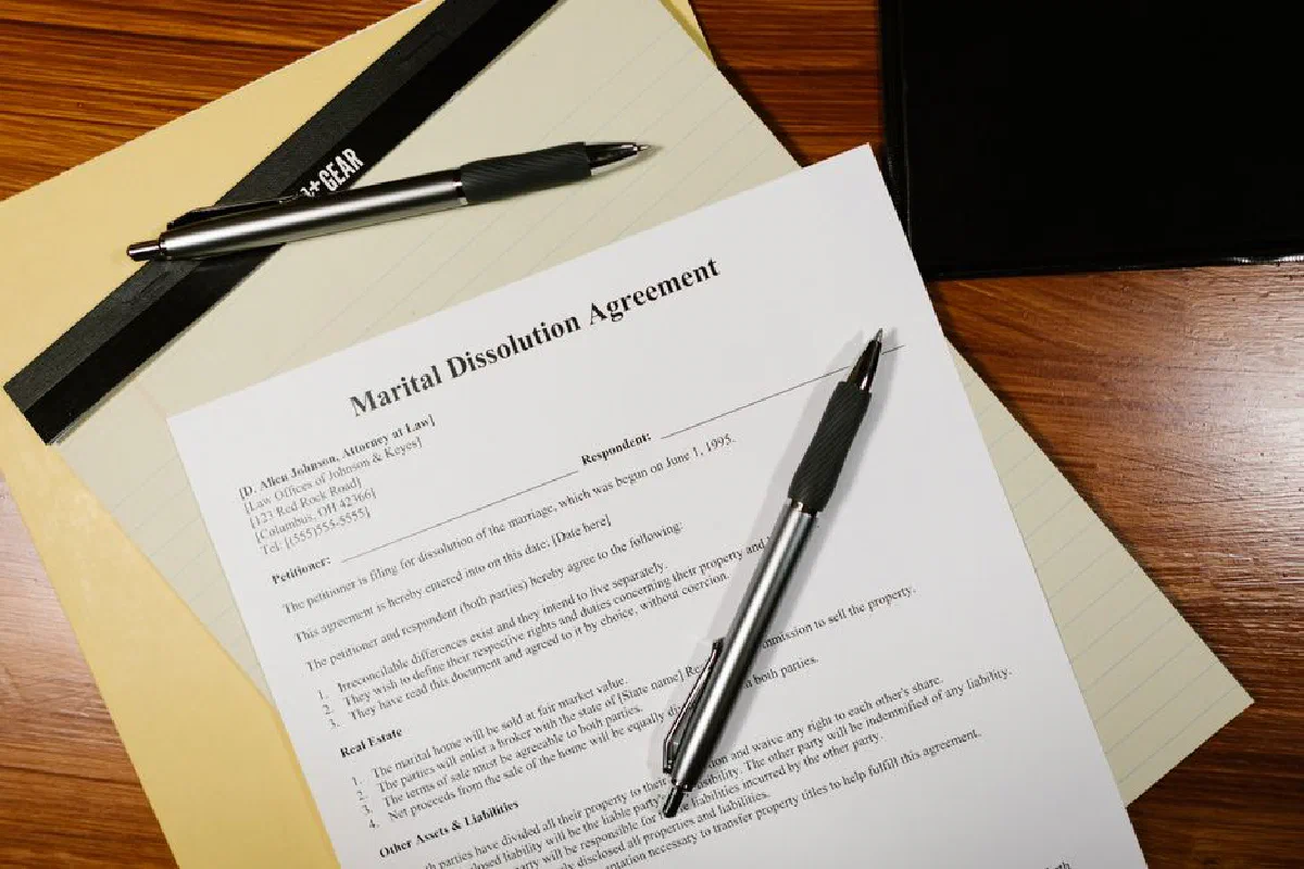 Flat lay of a marital dissolution agreement form with pens and files on a desk.
