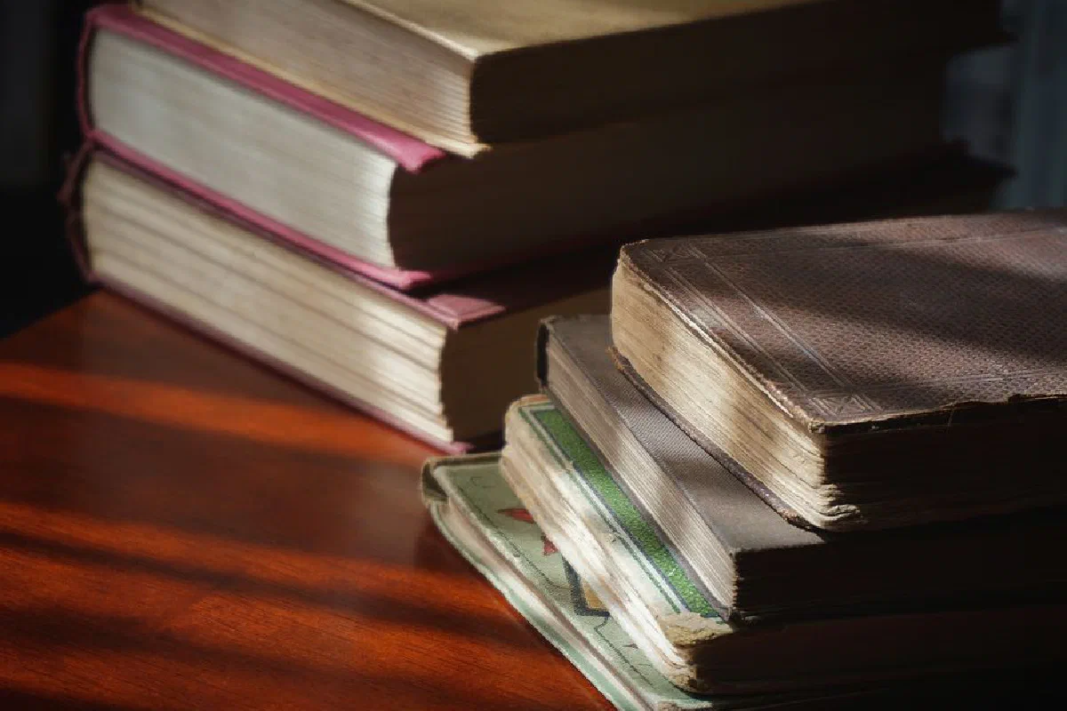 A close-up of vintage books stacked on a wooden table, showcasing aged pages and covers.