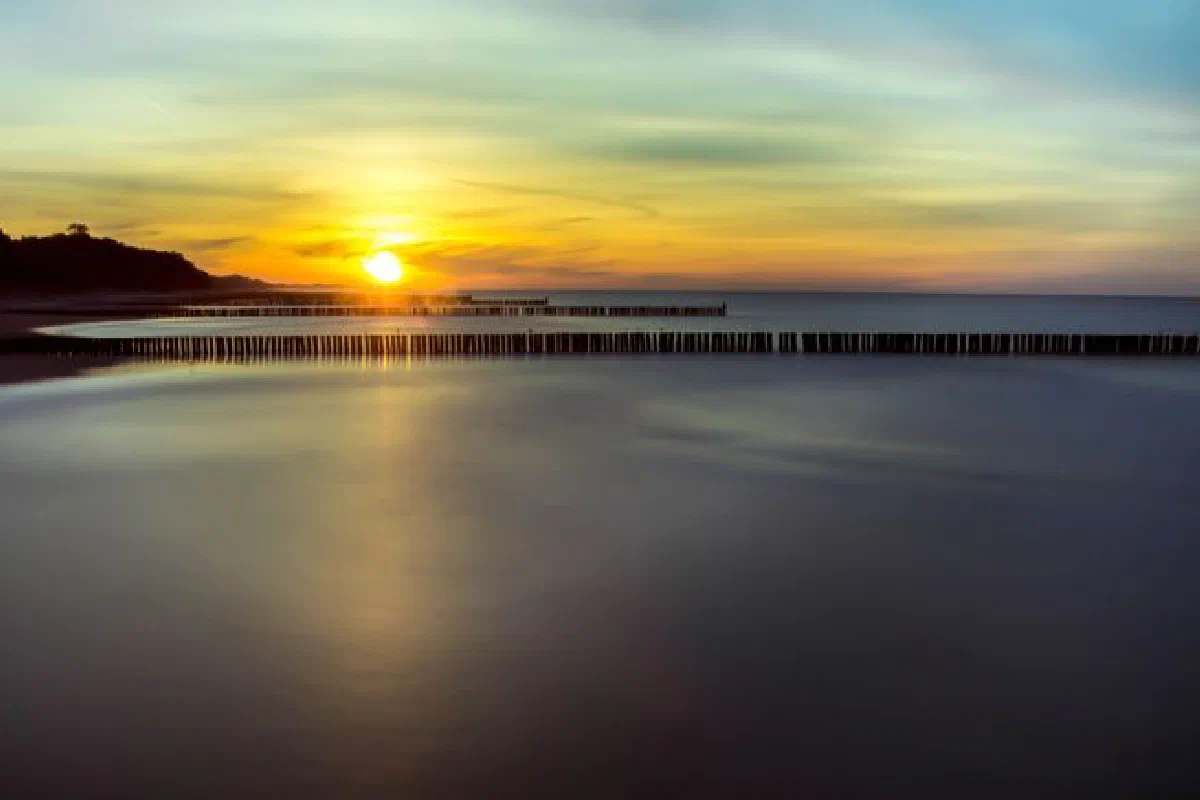 Serene ocean view at sunset with reflective water and silhouetted wooden jetties.