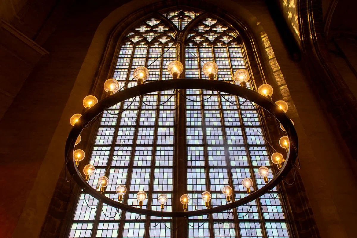 A stunning view of an ornate chandelier hanging beneath a large stained glass window in a historic church.