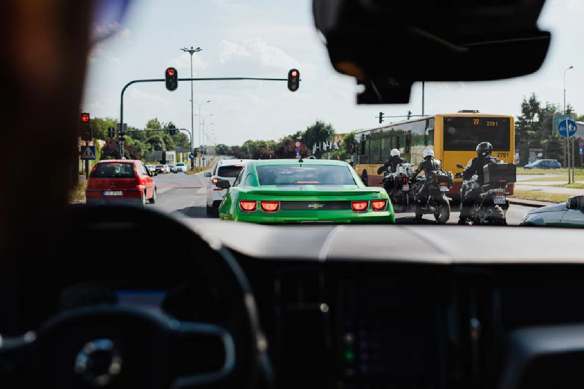 Street view of traffic with vehicles, bus, and motorcycles from a car's interior on a sunny day.