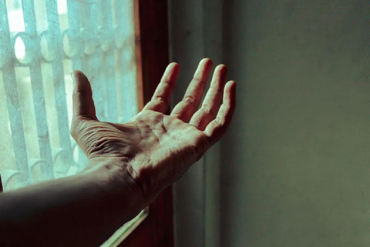 Close-up of a hand reaching out towards a window, illuminated by soft light.