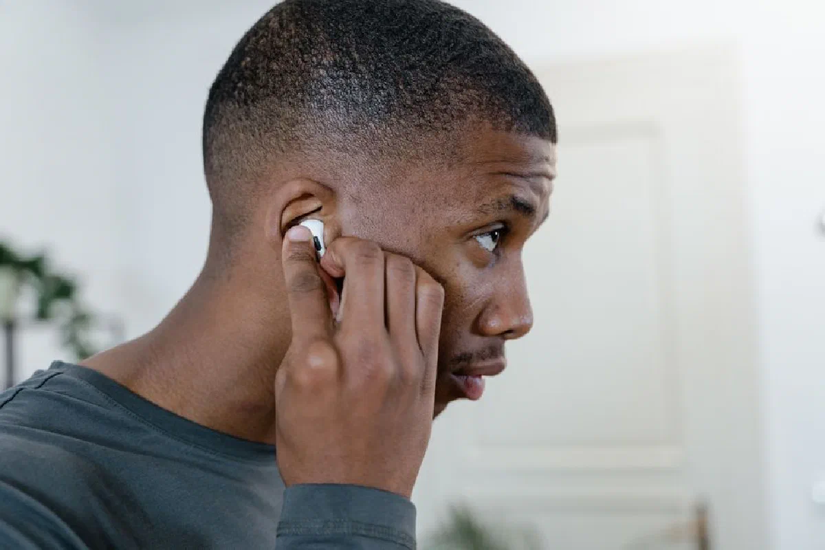 Close-up of a man adjusting his wireless earbuds while indoors, showcasing modern lifestyle.