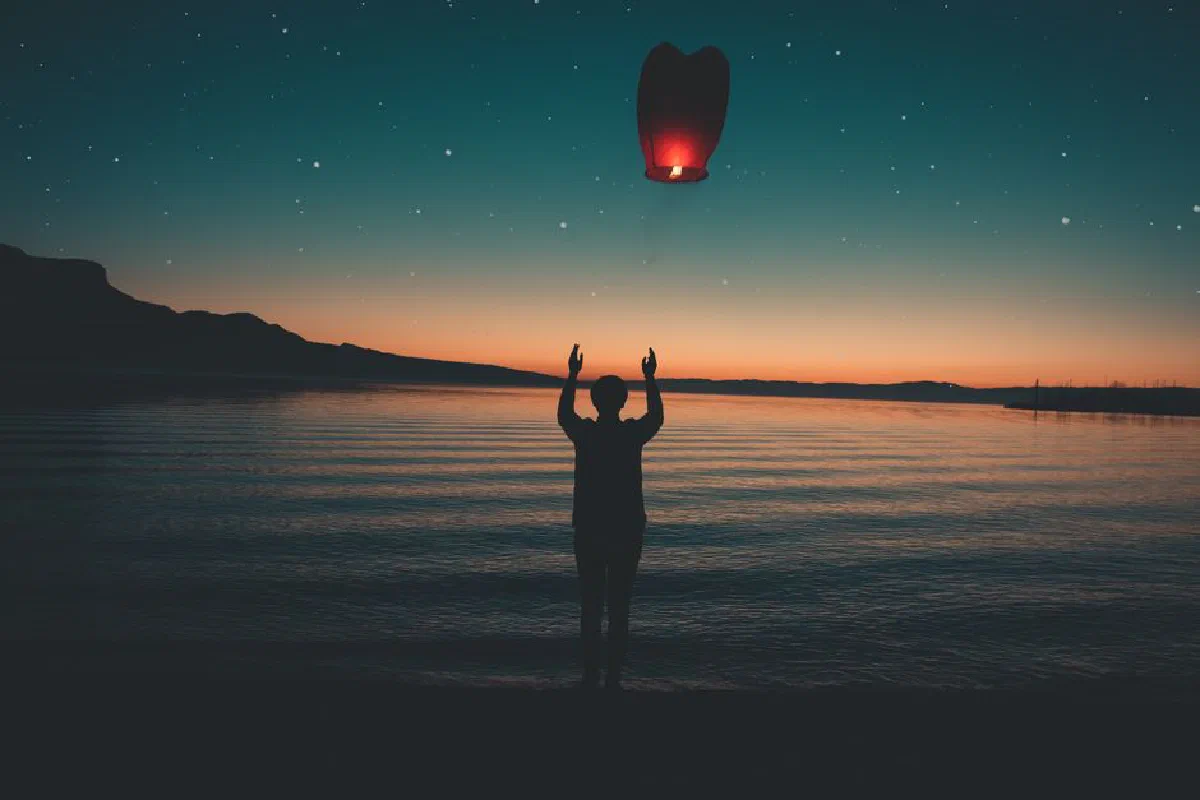 Silhouette releasing a floating lantern by a peaceful lake at sunset, creating a serene and magical atmosphere.