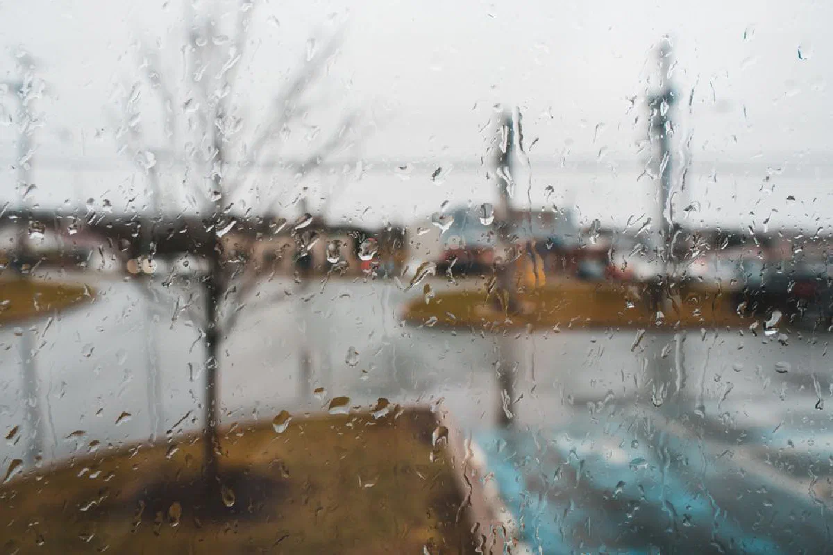 Glass wall with transparent aqua drips and fluids against urban street on rainy day in autumn