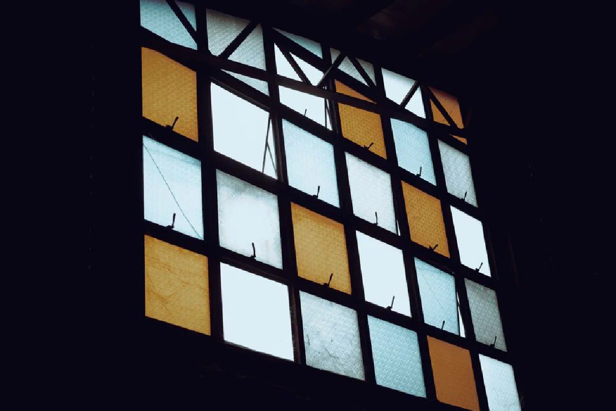 Aesthetic stained glass window with geometric patterns and warm colors in a dimly lit setting.