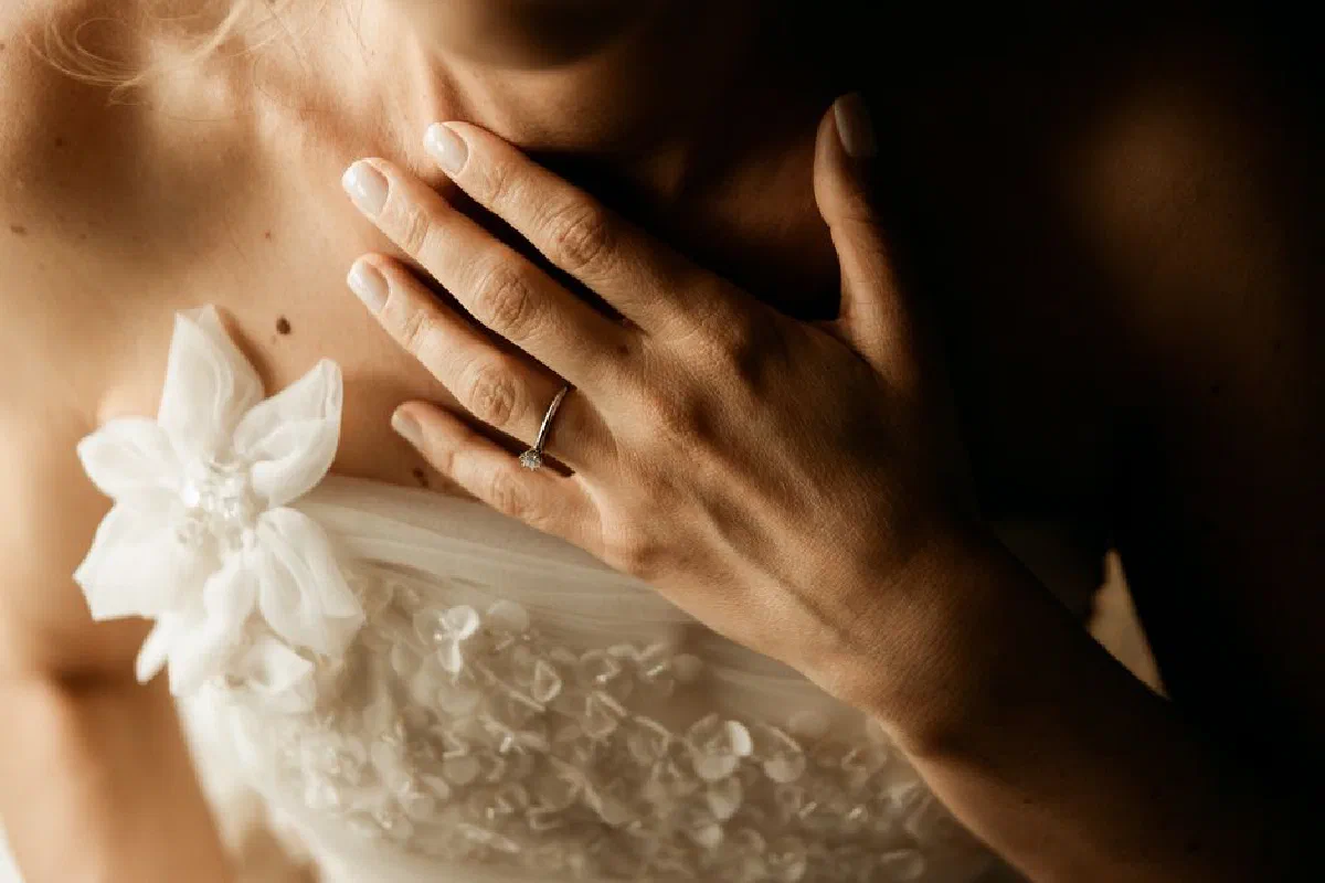 Close-up of a bride's hand with engagement ring on her wedding dress, conveying elegance and romance.