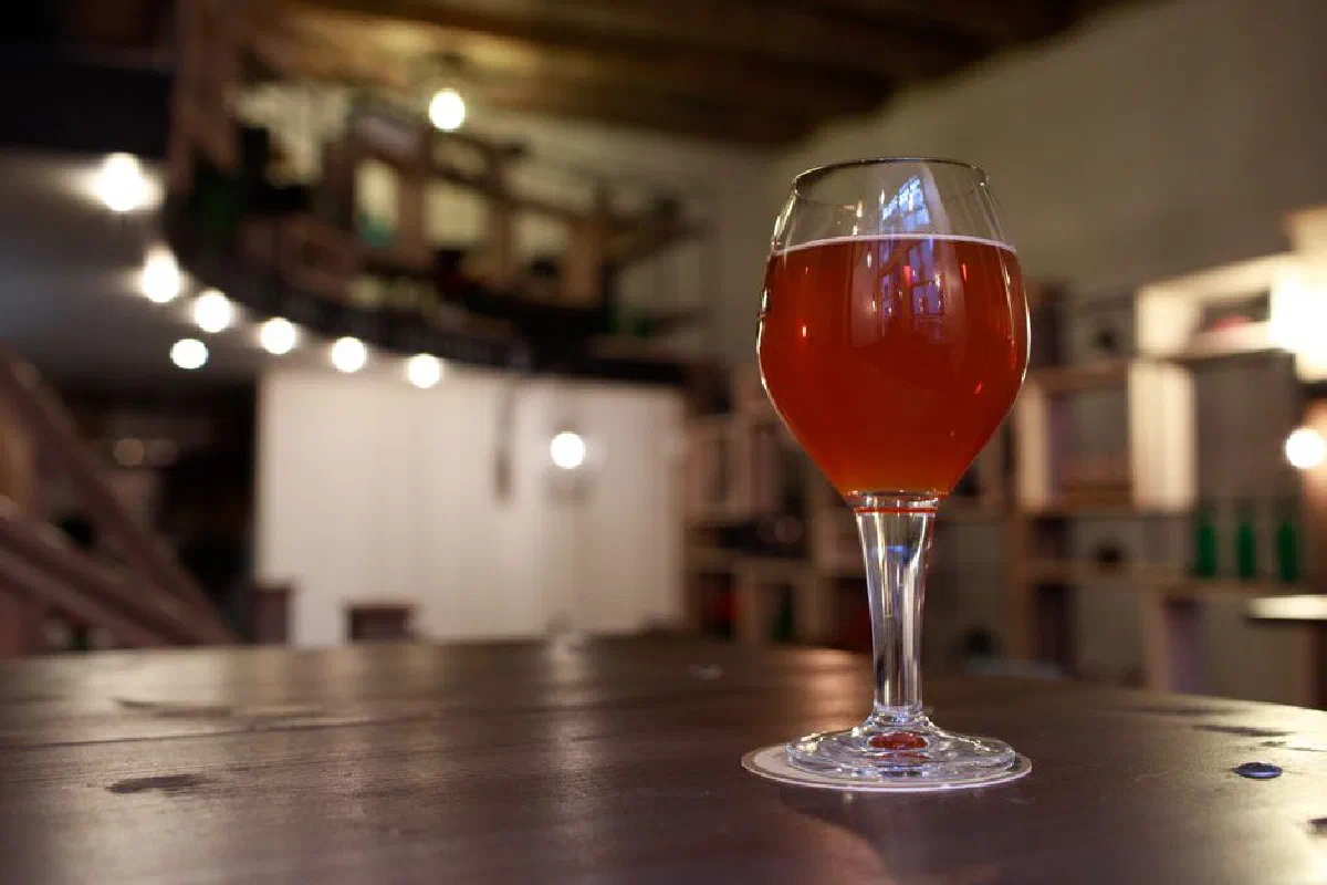 A beautifully lit glass of amber beer on a wooden table in a cozy bar setting, perfect for advertising.