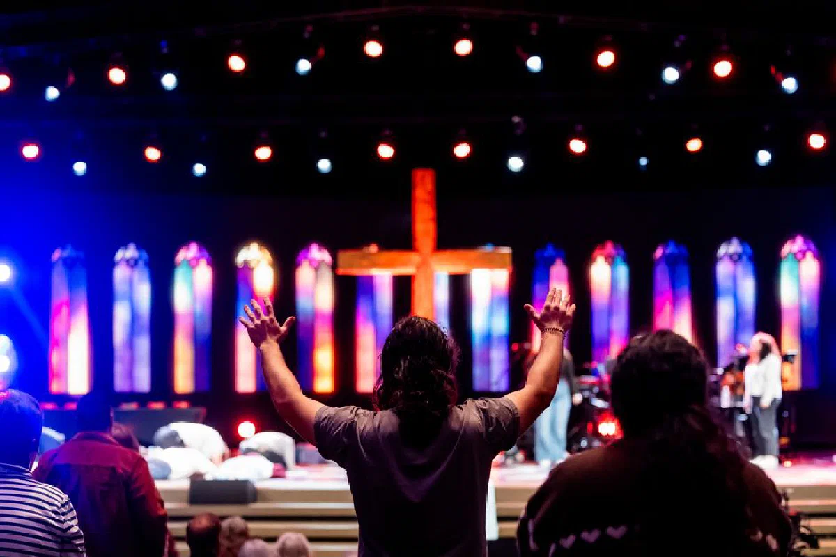 Lively church service with congregation worshipping under colorful stained-glass lighting.