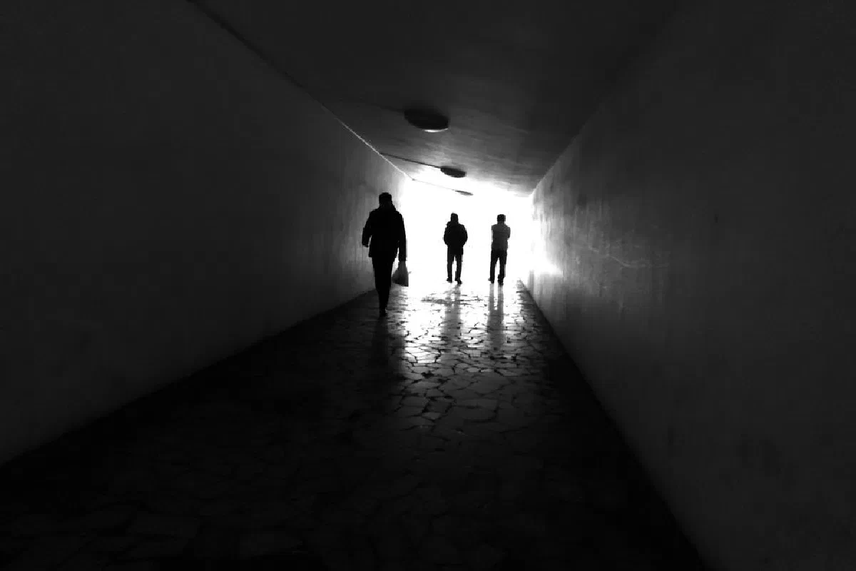 Three people silhouetted in an urban tunnel with striking light contrast.