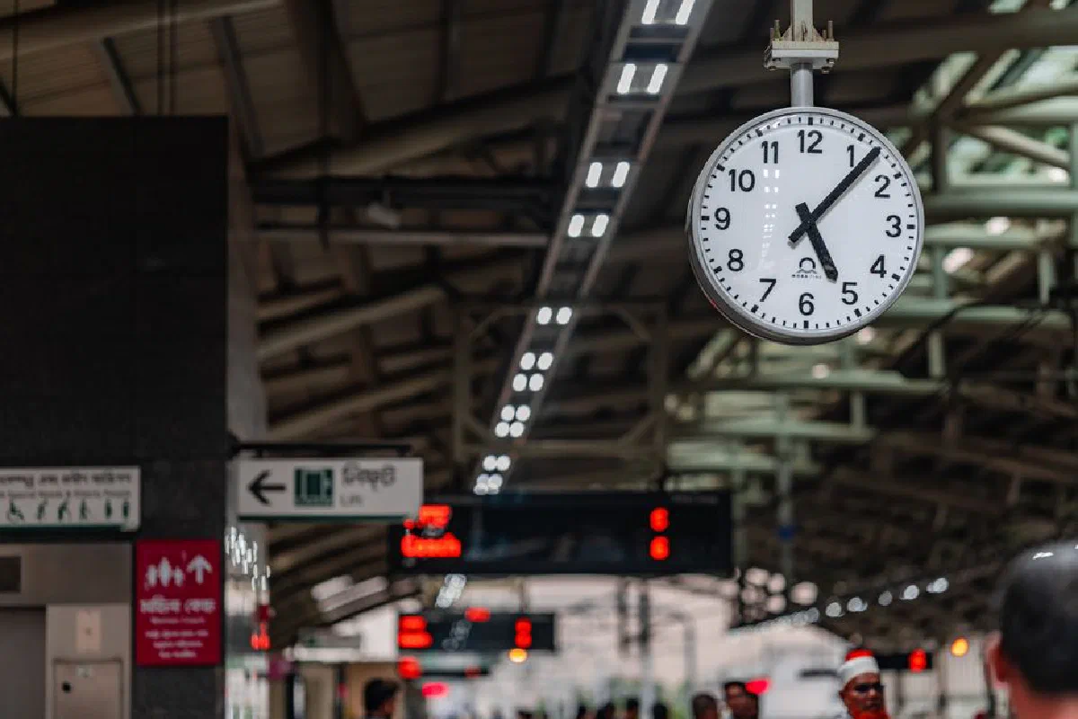 A large clock hangs prominently in a busy train station in Dhaka, Bangladesh, capturing the urban commute atmosphere.