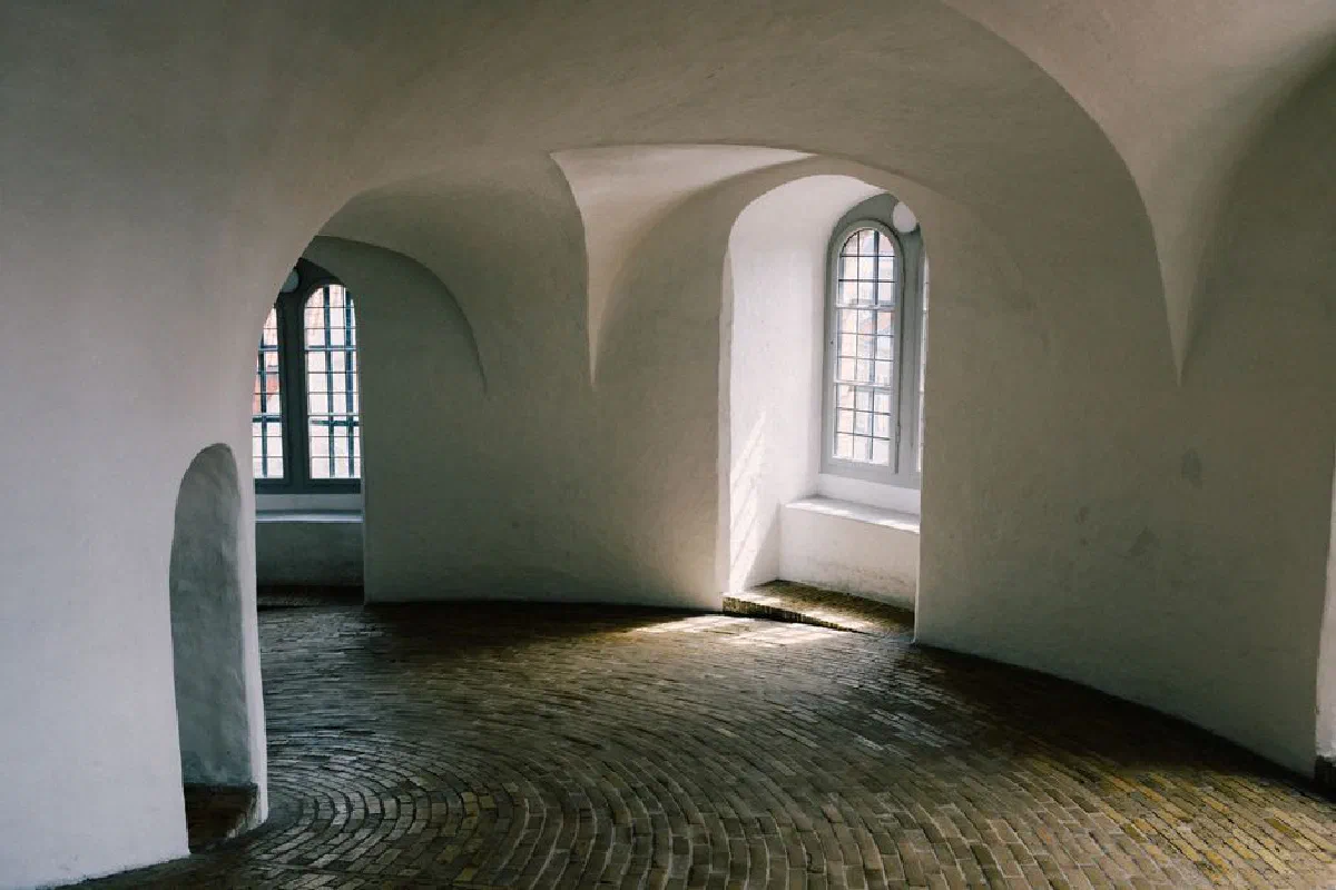 A beautifully lit curved hallway with a brick floor and arched windows, showcasing minimalist interior design.