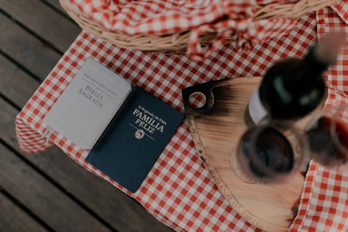 A rustic picnic table with plaid cloth, featuring books and wine for a cozy outdoor gathering.