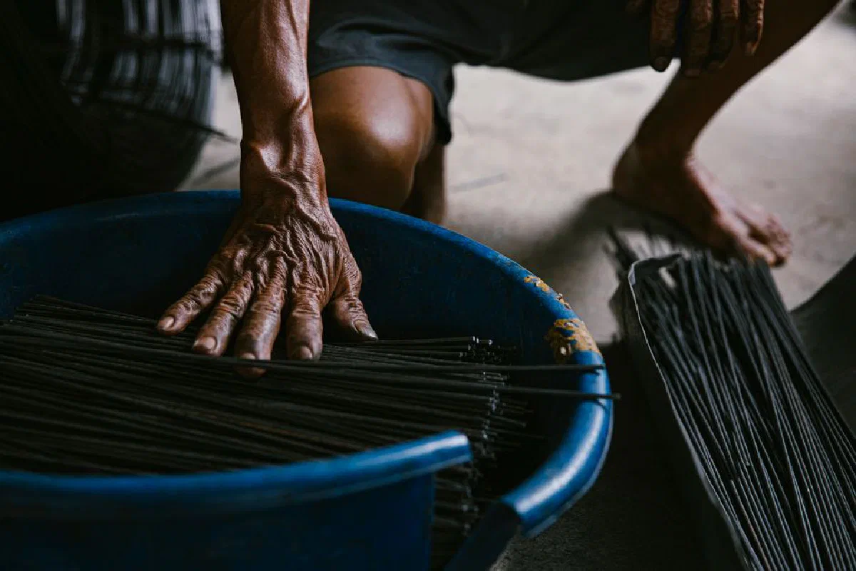 Close-up of an artisan's hands crafting incense sticks in a rustic indoor setting.