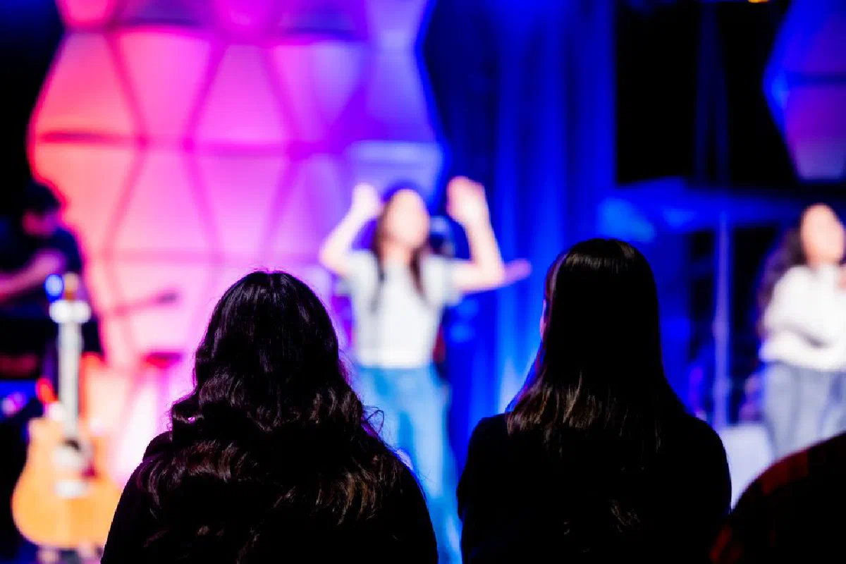 Silhouettes watching a vibrant concert with colorful lights on stage.