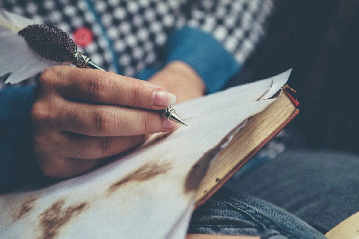 Close-up of a person using a quill pen to write in a vintage notebook.