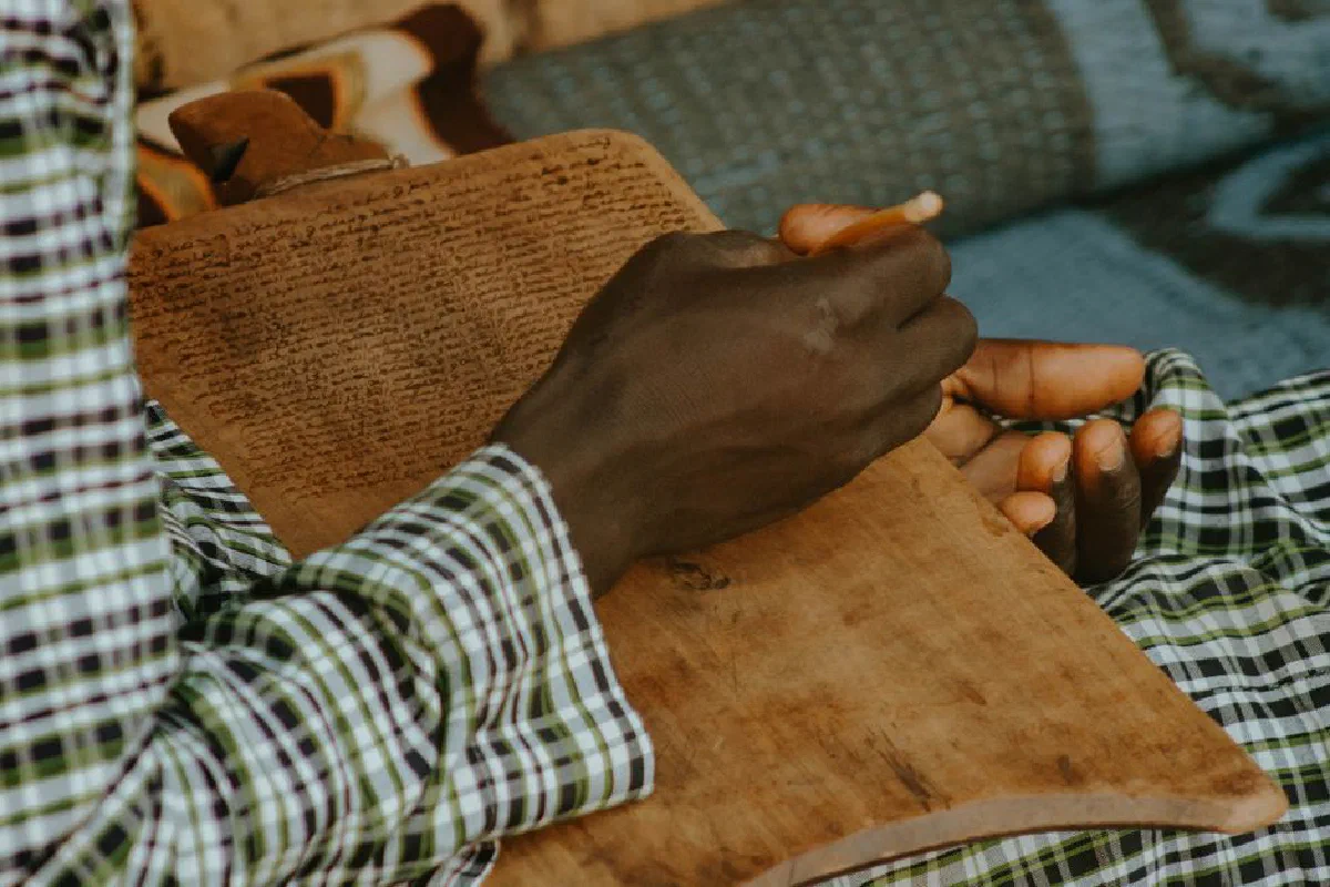 A person writes with a stylus on a traditional wooden tablet, showcasing ancient study practices.
