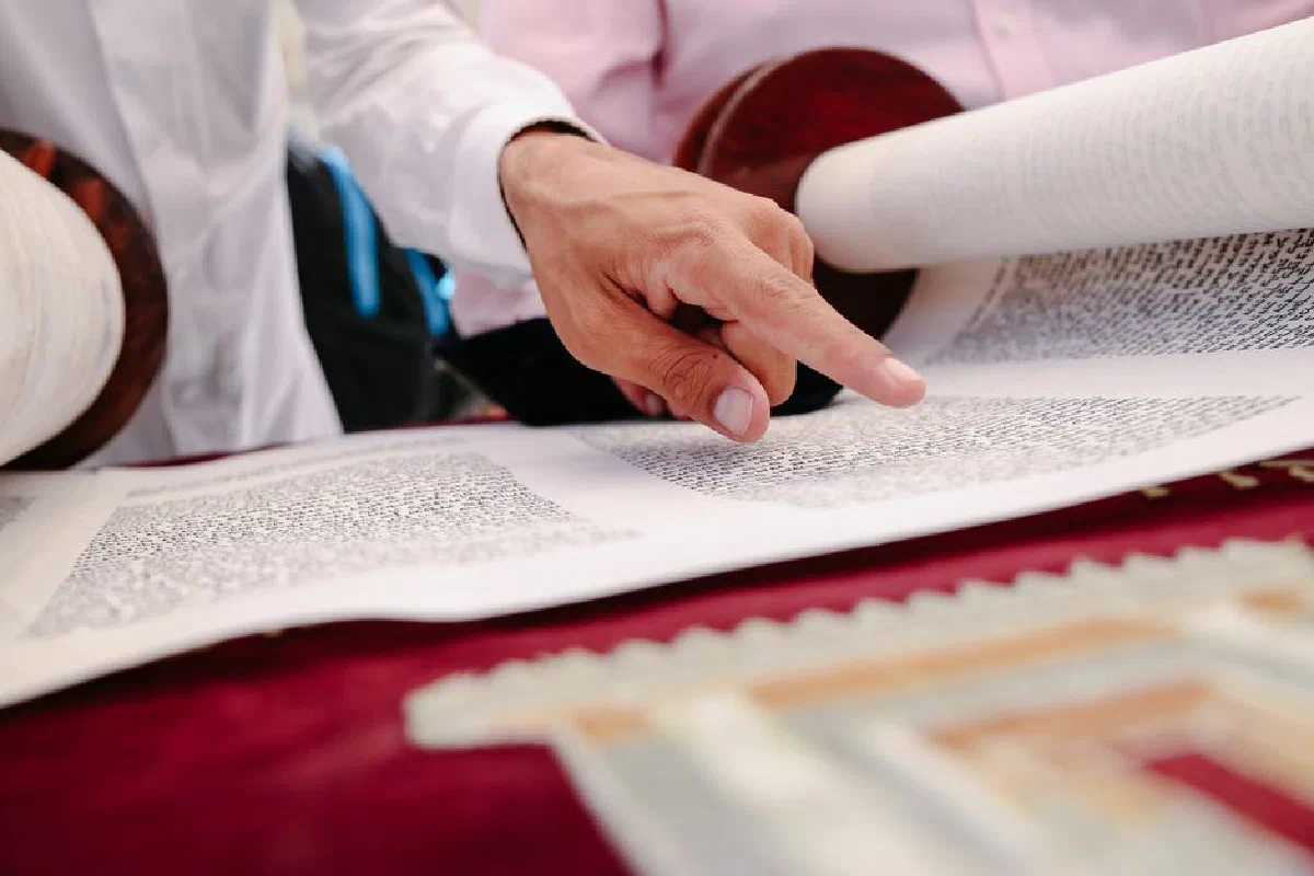 Detailed close-up of a hand pointing at an open Torah scroll, symbolizing Jewish religious practices.