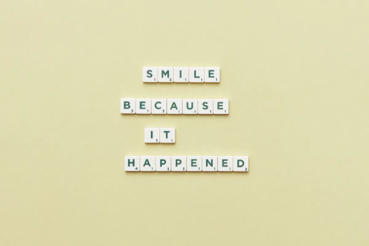 Scrabble tiles arranged to say 'Smile because it happened' on a pastel background, offering a motivational message.