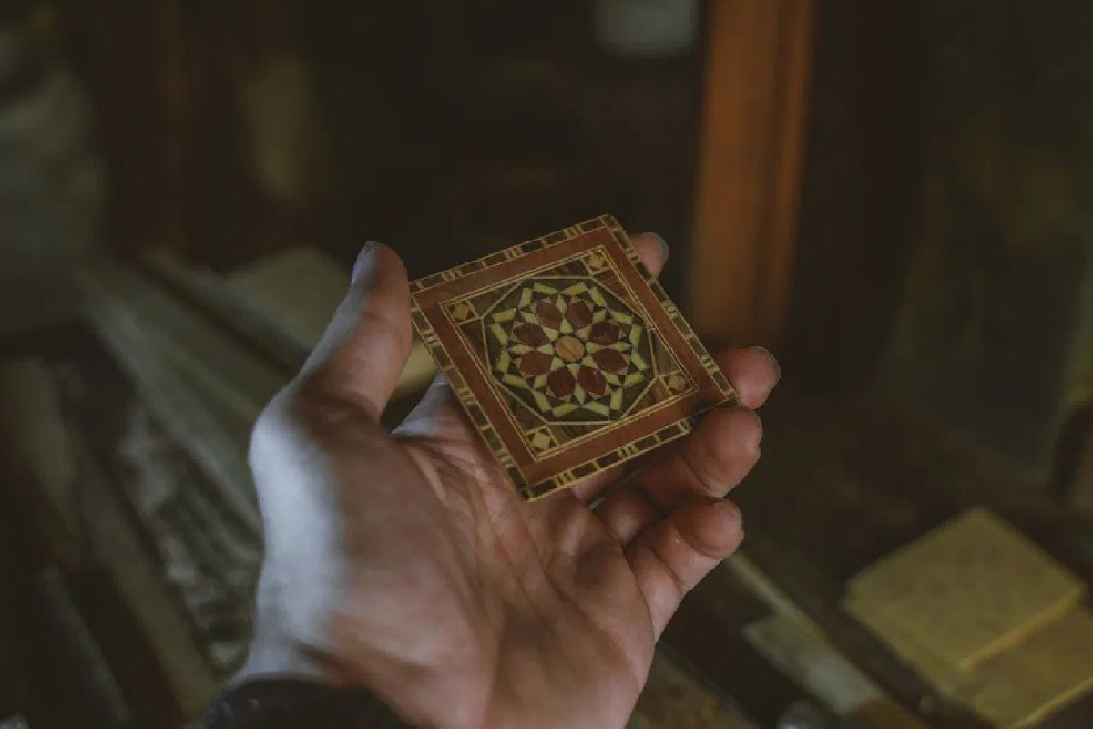A hand holds a detailed mosaic piece showcasing traditional Syrian craftsmanship in Damascus.