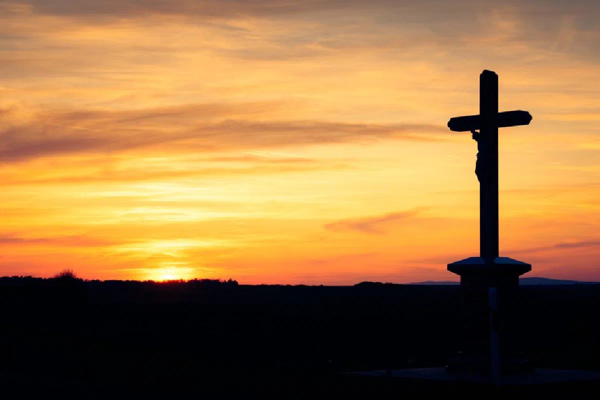 Silhouette of a cross against a vibrant sunset sky, capturing tranquil scenery.